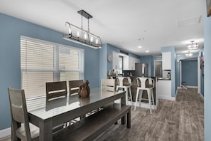 A modern kitchen with white cabinets, a dining area with a glass-top table, and a built-in bench.
