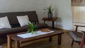 A living room with a sofa, a coffee table, a chair, a plant, and a shelf with books and candles. - Casa Cedro in Luddui (Budoni)