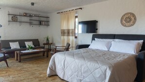 A bedroom with a bed, a sofa, a chair, a small table, and a TV. - Casa Cedro in Luddui (Budoni)