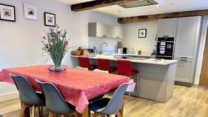 Une cuisine moderne avec des meubles blancs, un îlot central doté de chaises rouges et un coin repas avec une nappe rouge.
