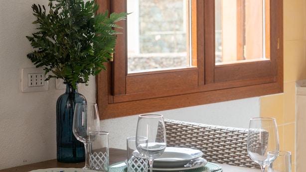 Une table à manger dressée avec des assiettes, des verres et un vase contenant des feuilles vertes.