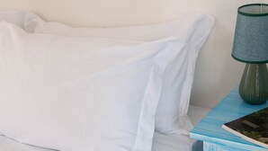 Un lit avec une literie blanche, un oreiller à motifs verts et blancs, et une table de chevet bleue avec une lampe et un livre.