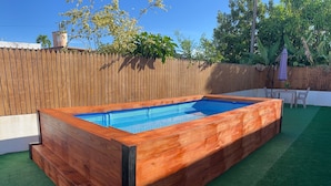 A rectangular wooden swimming pool with a blue tiled interior, surrounded by artificial green turf. - Garden Studio With Yard Space Near Mall & Airport (Carolina)