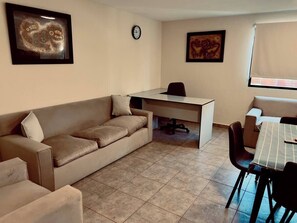 Cozy living space with a sofa, dining table, and desk area, complete with a clock and artwork.