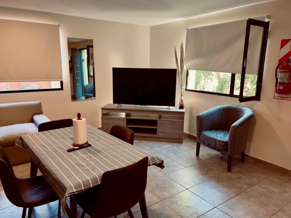 Relax in this stylish living room with a large flat-screen TV, dining table, and comfortable armchair.