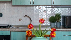 A kitchen with teal cabinets, a sink, a stove, and a microwave. There is a teal vase with tulips on a wooden table. - La Casa di Salvatore (Budoni)