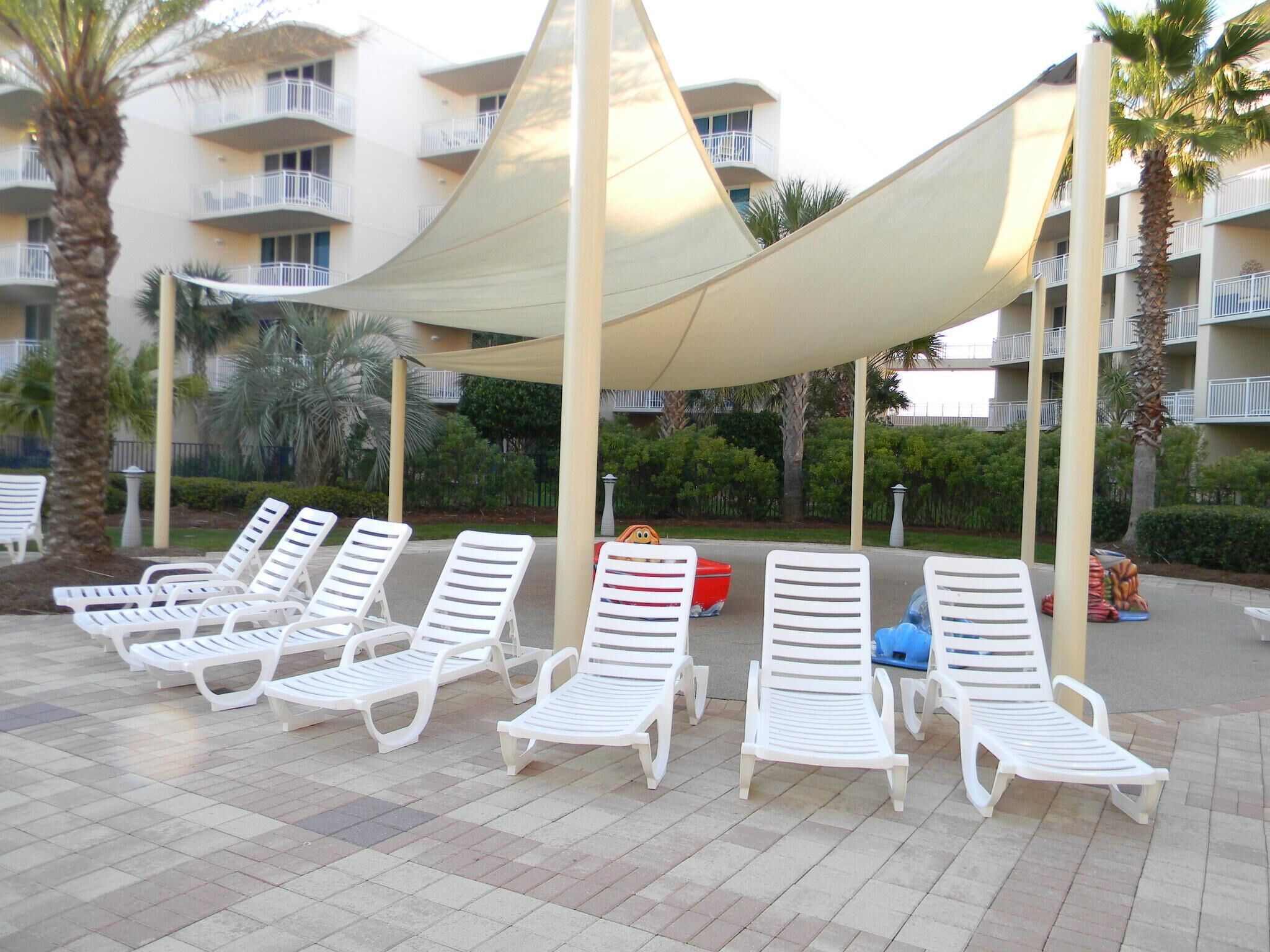 Un espace aménagé au bord de la piscine, avec des chaises longues blanches et un auvent.