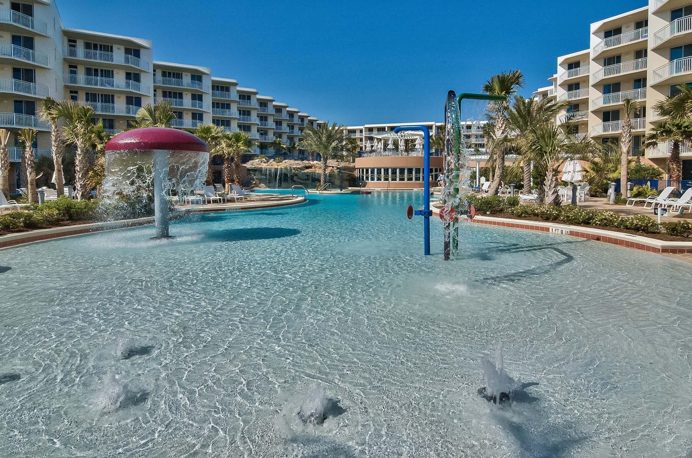 A hotel pool area with clear water, palm trees, and a water feature.
