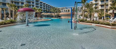 A hotel pool area with clear water, palm trees, and a water feature.