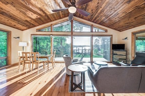 A spacious room with wooden flooring, a ceiling fan, large windows, and a dining area with chairs and a table. - Waterfront Lancaster Cabin ~ 10 Mi to Kilmarnock! (Lancaster)