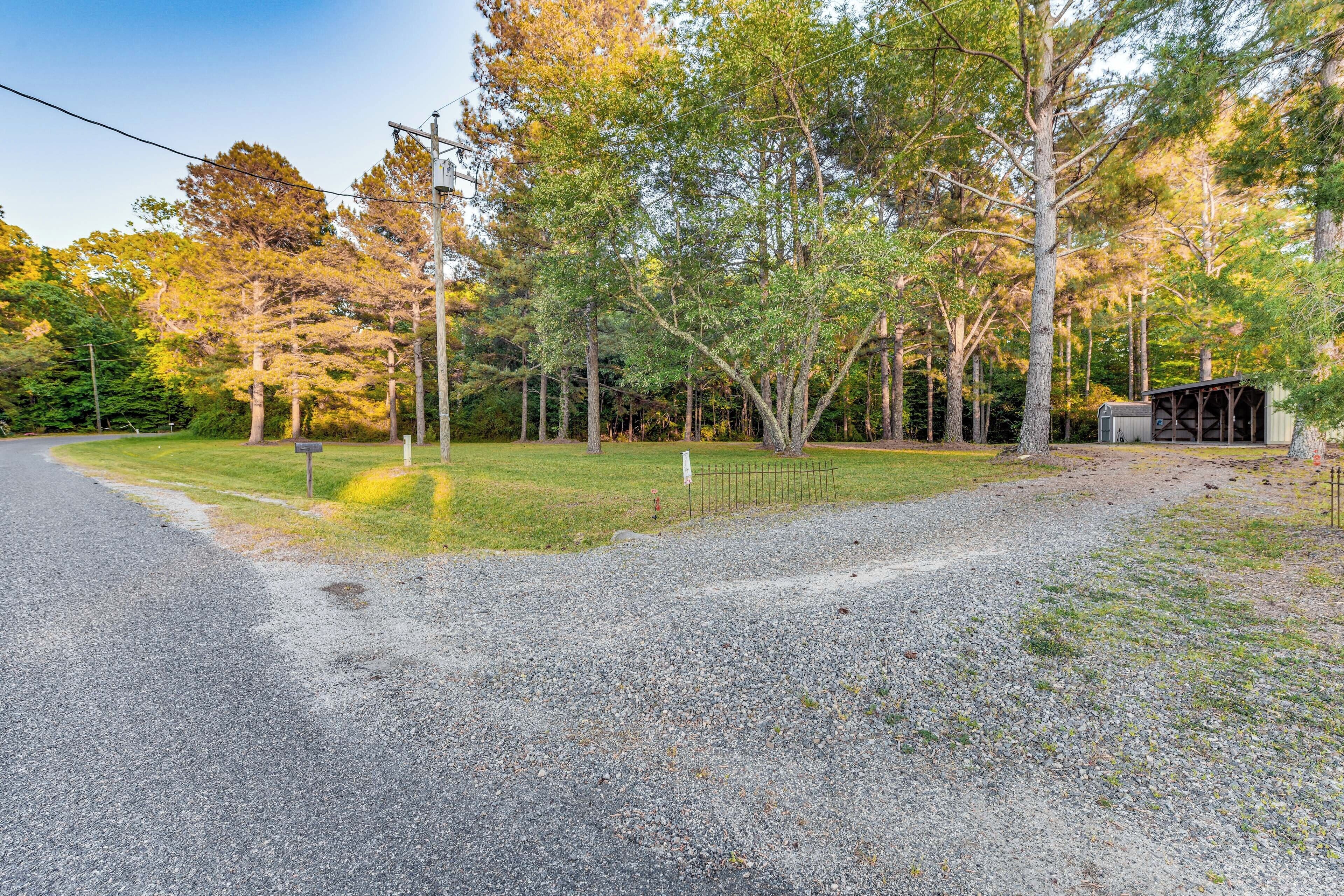 A gravel driveway leading to a covered structure in a wooded area.