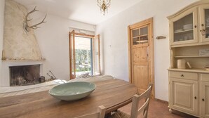 Een eetgedeelte met een houten tafel, stoelen, een grote schaal, een open haard en een kast met glazen deuren.