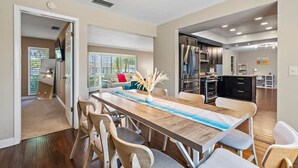 A spacious dining area with a long wooden table, modern kitchen with stainless steel appliances, and a cozy living room with a sofa and large windows.
