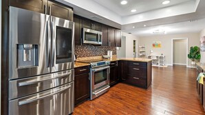 A modern kitchen with stainless steel appliances, dark wood cabinets, and a wooden floor.