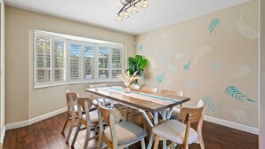 A dining area with a wooden table and chairs, a potted plant, and a window with shutters.