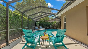 A covered outdoor area with a pool, green chairs, and a table.