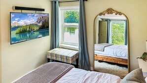 Un dormitorio con cama, mesita de noche, espejo y ventana con cortinas.