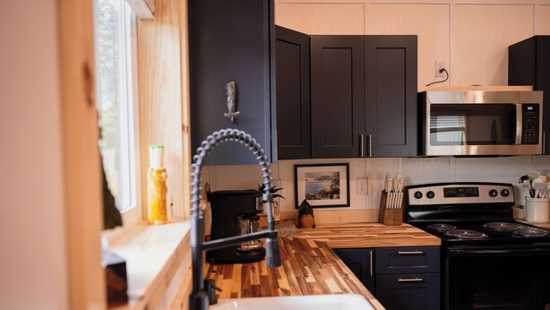 Une cuisine moderne avec des meubles de couleur sombre, un four à micro-ondes en acier inoxydable, une cuisinière et un plan de travail en bois.