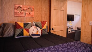 Une pièce comprenant un lit, un mur en bois orné de motifs sculptés et une porte donnant sur un espace cuisine.