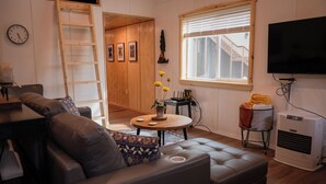 Un salon moderne avec un canapé en cuir, une table basse agrémentée d’objets décoratifs, un téléviseur et une fenêtre équipée de stores.