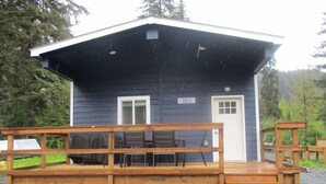 Une petite cabane avec une terrasse en bois et deux portes, dont l’une porte un numéro.
