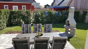 Une terrasse extérieure avec une table en pierre et quatre chaises, un barbecue et une haie en arrière-plan.