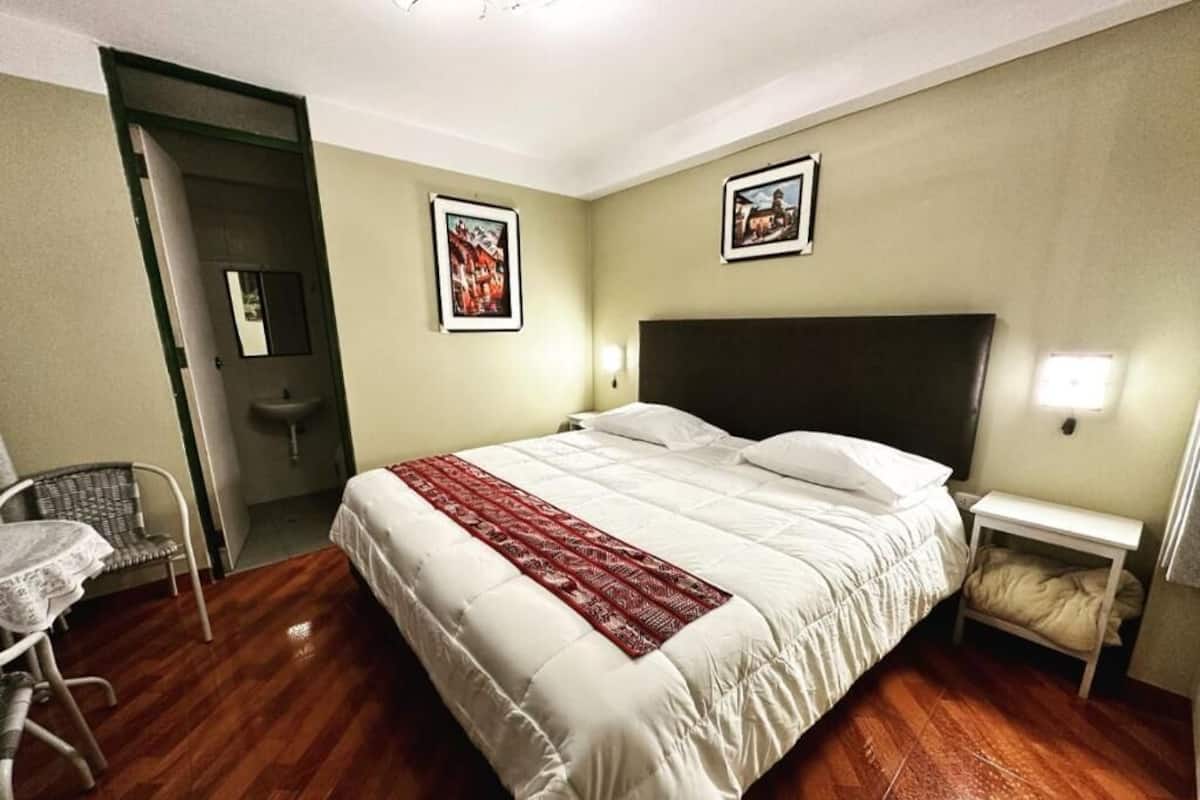 Habitación de hotel con una cama grande, una mesita de noche, una silla y una pequeña mesa.