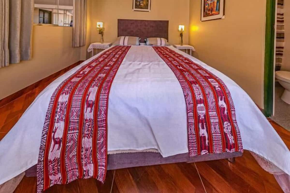 Habitación de hotel con una cama grande, dos lámparas de noche, un cuadro en la pared y una ventana con cortinas.