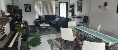 Ein Wohnzimmer mit Klavier, Sofa, Couchtisch und Esstisch mit Stühlen.