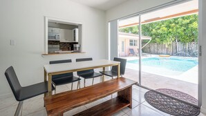 Angolo ristoro con tavolo e sedie, cucina sullo sfondo e vista su una piscina esterna.