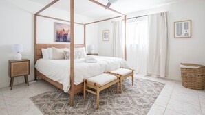 Un letto a baldacchino con zanzariera, una ventola a soffitto, un comodino con una lampada e un cesto di vimini sul pavimento.