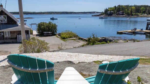 A view from a porch with two green Adirondack chairs and a white table, overlooking a calm lake with several boats and a dock. - Cozy Ocean Side Cottage with screened in Sun room! 5 minutes from Private beach (Georgetown)