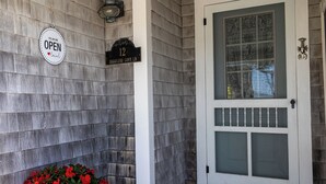 A house entrance with a wooden exterior, a white door with glass panels, a number sign '12', and a 'YES WE ARE OPEN' sign. - Cozy Ocean Side Cottage with screened in Sun room! 5 minutes from Private beach (Georgetown)