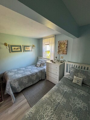 A bedroom with two beds, a dresser, and a window with curtains.