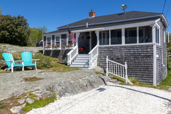 A two-story house with a porch, a flag, and a stone pathway leading to the entrance.