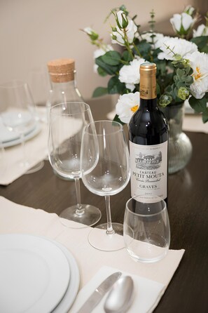 A table set with white plates, wine glasses, and a bottle of Chateau Petit Moutau Graves 2021 wine. - Unique Luxury Central Flat (Brussels)