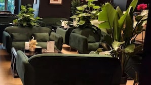 A seating area with green upholstered sofas, a small table with a menu, and potted plants. - Vienna International Hotel (Chengdu)