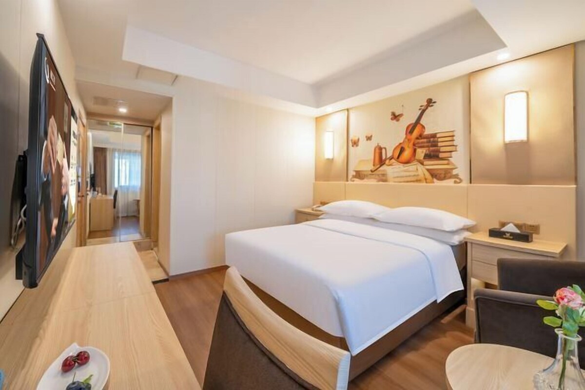 A hotel room with a bed, bedside table, and a wall with a musical instrument and books.