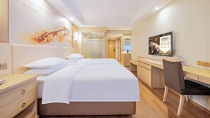 A hotel room with a bed, a desk, and a chair. There is a television on the desk and a poster on the wall. - Vienna International Hotel (Chengdu)
