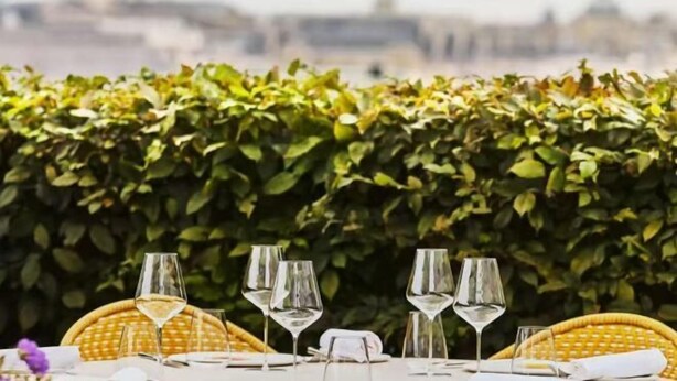 A table set with wine glasses and a wicker chair, with a cityscape in the background. - Vienna International Hotel (Chengdu)