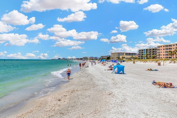 A beach with clear skies, a sandy shore, and buildings in the background. - Gorgeous water front condo in Madeira Beach (Madeira Beach)