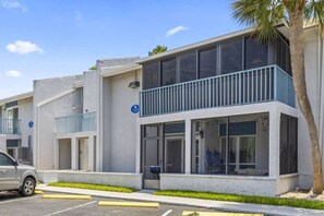 A modern building with a balcony, large windows, and a parking area.