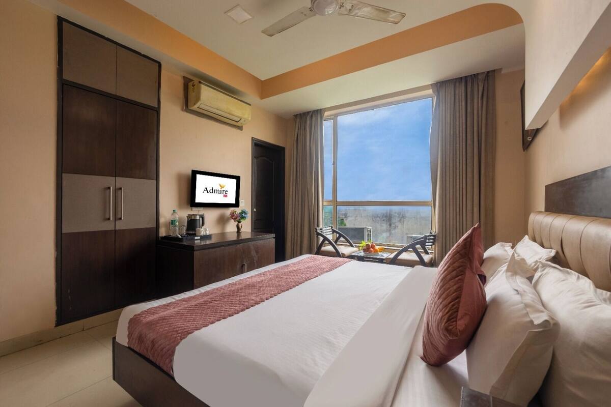 A hotel room with a bed, a desk with a TV, a window with a view, and a wardrobe.