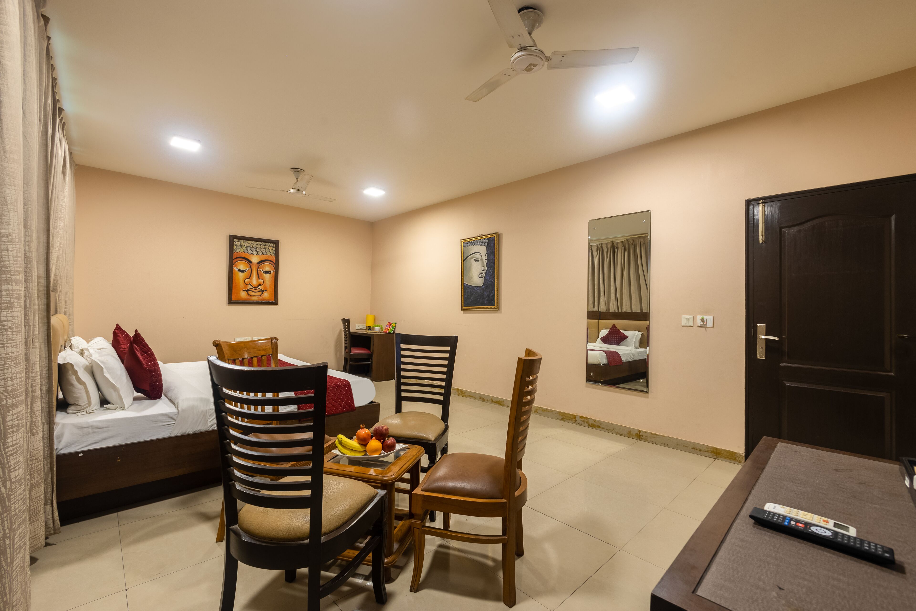 A hotel room with a bed, a dining table with chairs, a ceiling fan, and a TV.