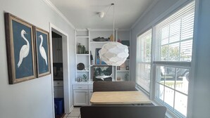 Una habitación con cama, escritorio y ventana. Hay dos cuadros en la pared, un tapete en el suelo y una lámpara en el techo.