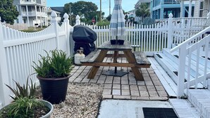Un patio con mesa de picnic, plantas en macetas y cerca blanca de piquetes.