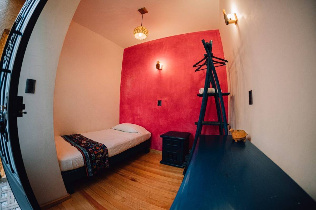 A compact room with a single bed, a small table, a ladder, and a wall-mounted light fixture.