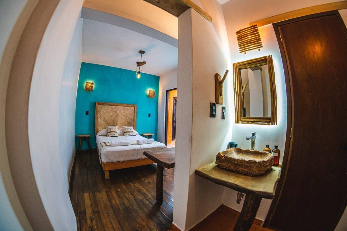 A room with a bed, wooden floor, a stone sink, and a mirror.