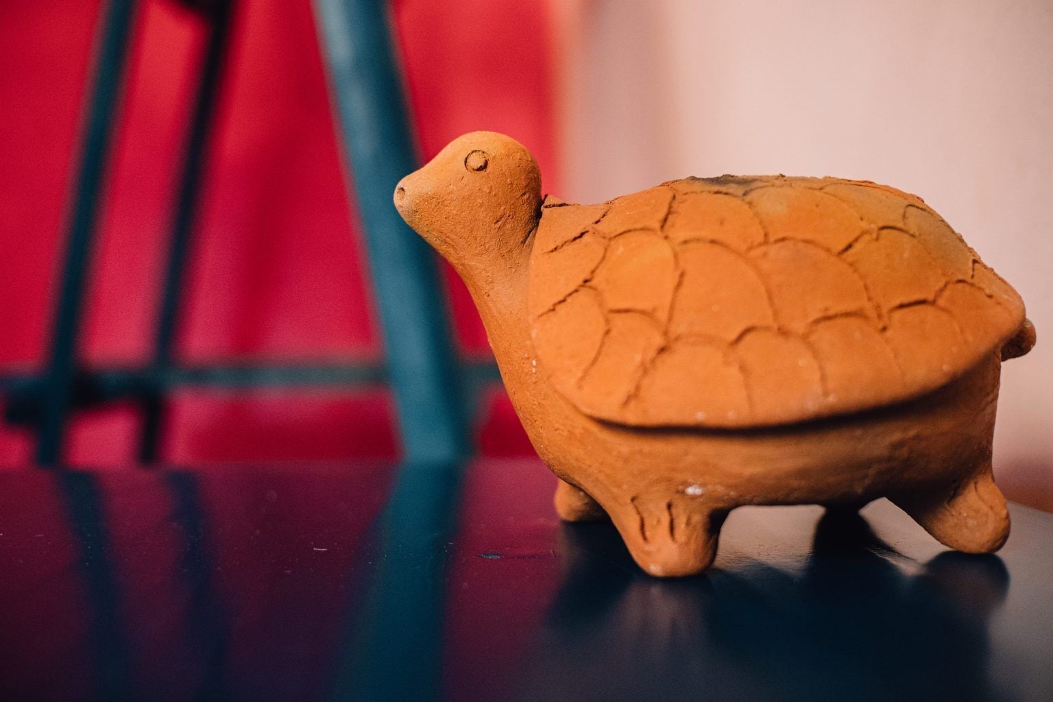 Una figurita de tortuga de terracota sobre una superficie oscura con un fondo rojo desenfocado.