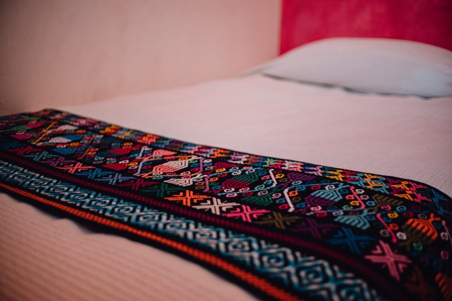 A colorful embroidered fabric laid on a bed with a white pillow.